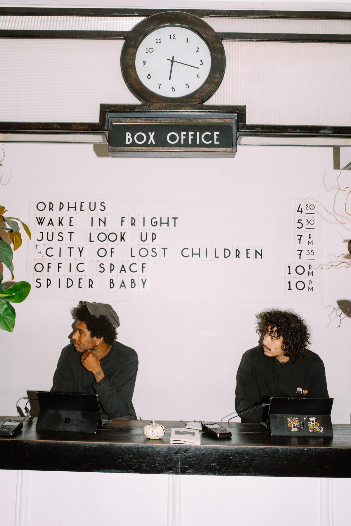Box office attendants under the Metrograph clock, with the Just Look Up showtime on the board