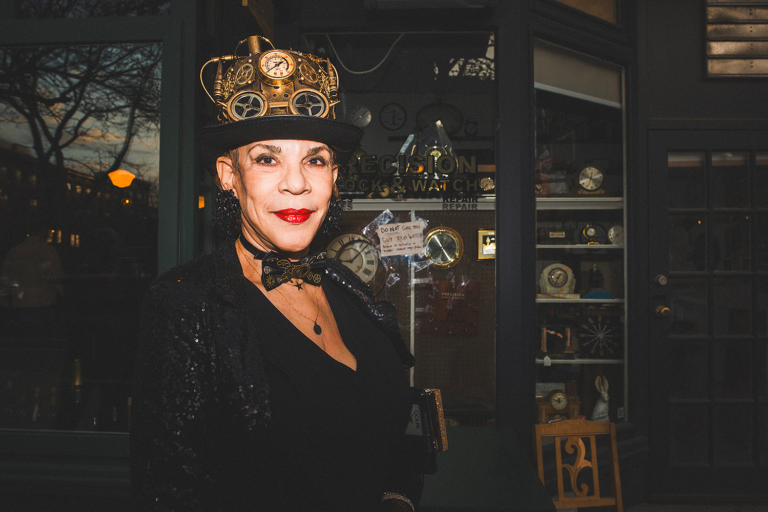 Woman in a steampunk top hat outside the clock and watch shop window