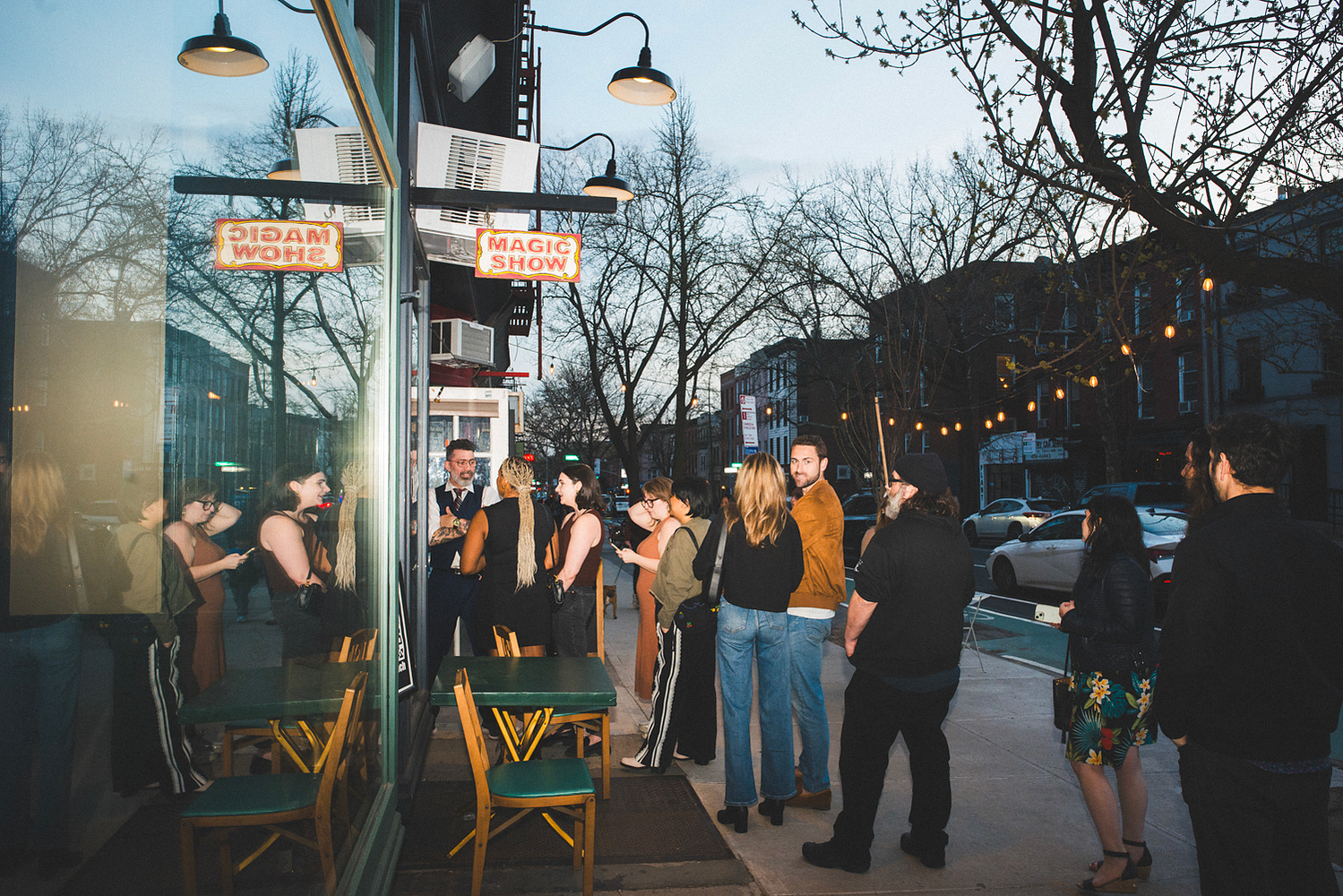 Crowd gathering on the sidewalk under the Magic Show sign at dusk