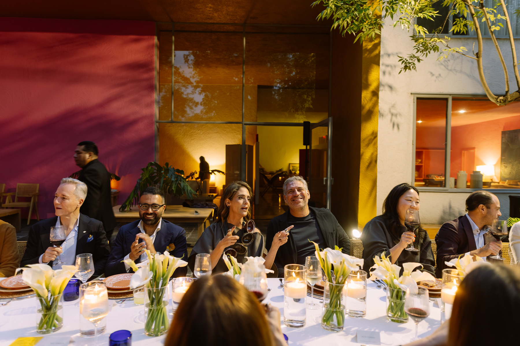 Guests laughing at the dinner table, calla lilies in the foreground