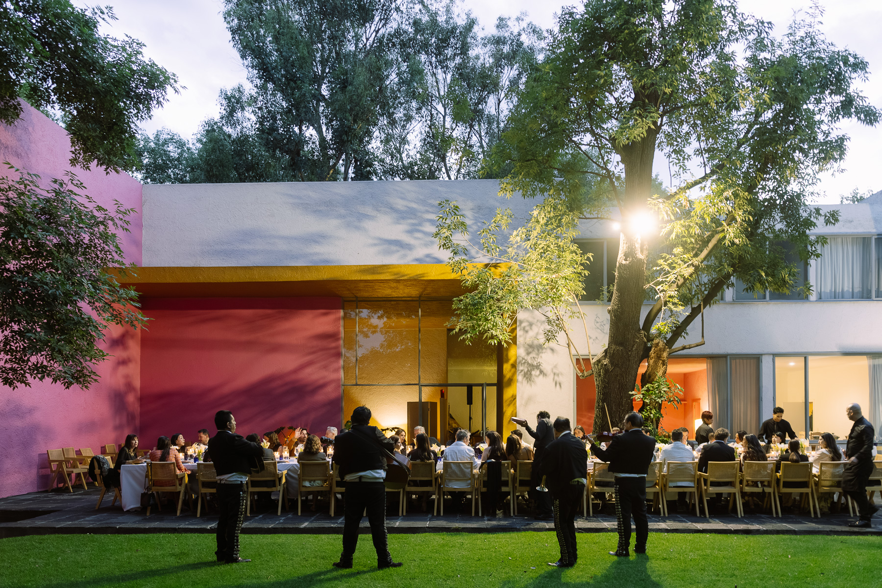 Long table dinner in the garden, house lit at dusk