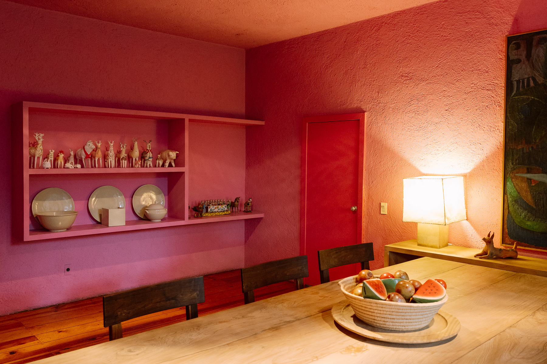 Pink dining room with a pottery shelf and a bowl of watermelon